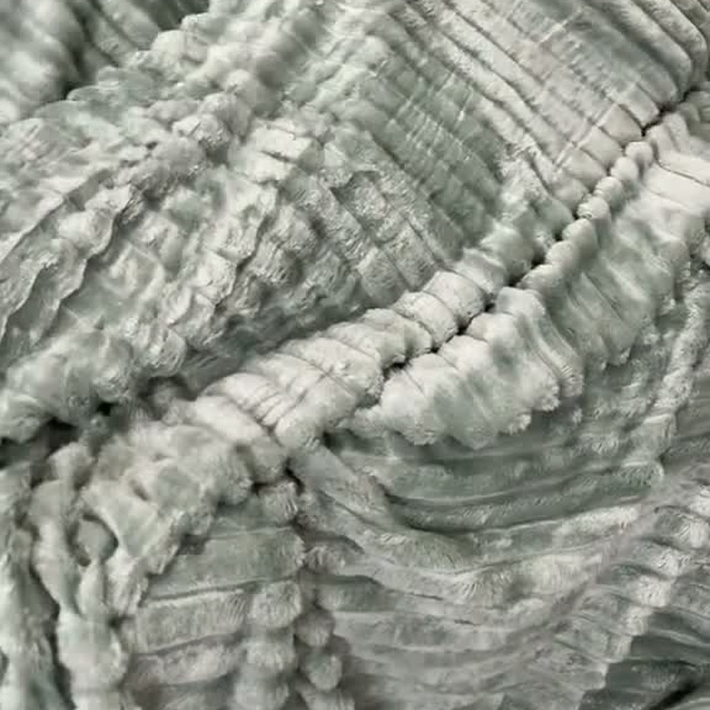 The Sage green ribbed-stripe plush blanket wrapped around a person on a couch