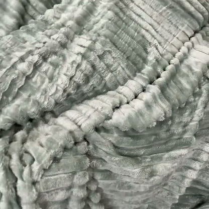 The Sage green ribbed-stripe plush blanket wrapped around a person on a couch