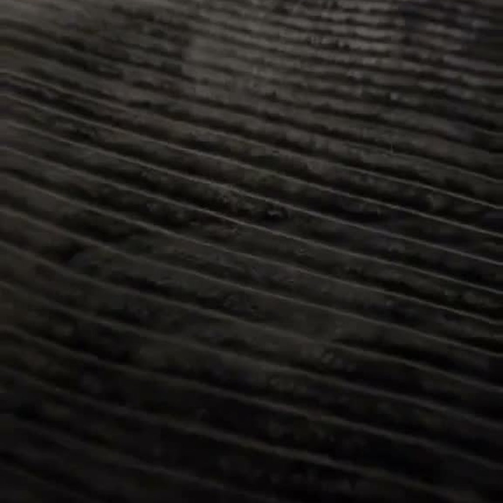 The Charcoal ribbed-stripe plush blanket on a bed