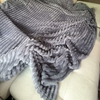 The real Grey blanket lies in ribbed folds over a cream couch.