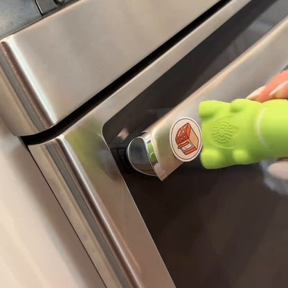 A hand touches the green dinosaur reader base to a learning sticker on an oven door.