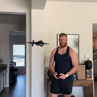 man in a black tank top flying the jet in his living room, the jet in the air above him