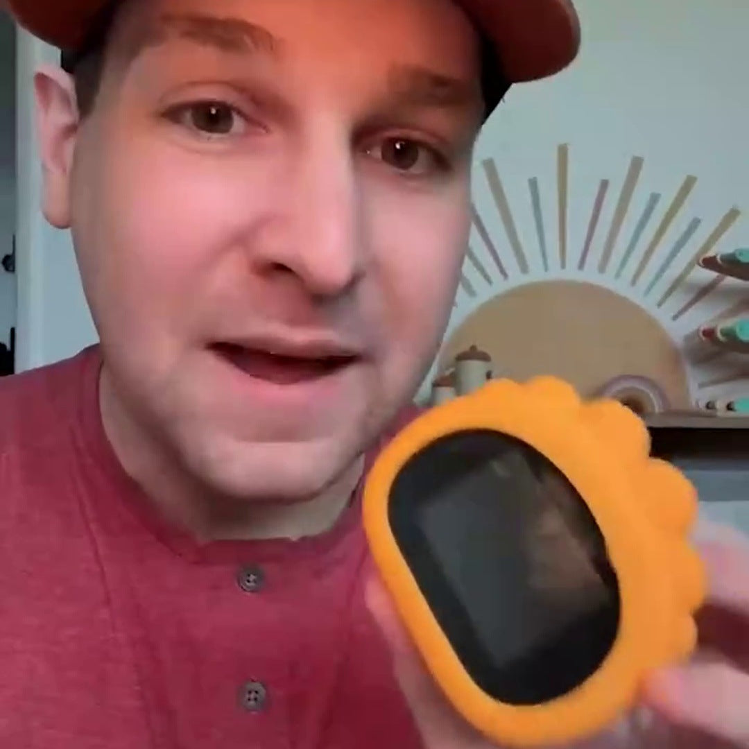 A dad in a brown cap and red shirt holds the yellow scope toward the camera, its screen lit, in his living room