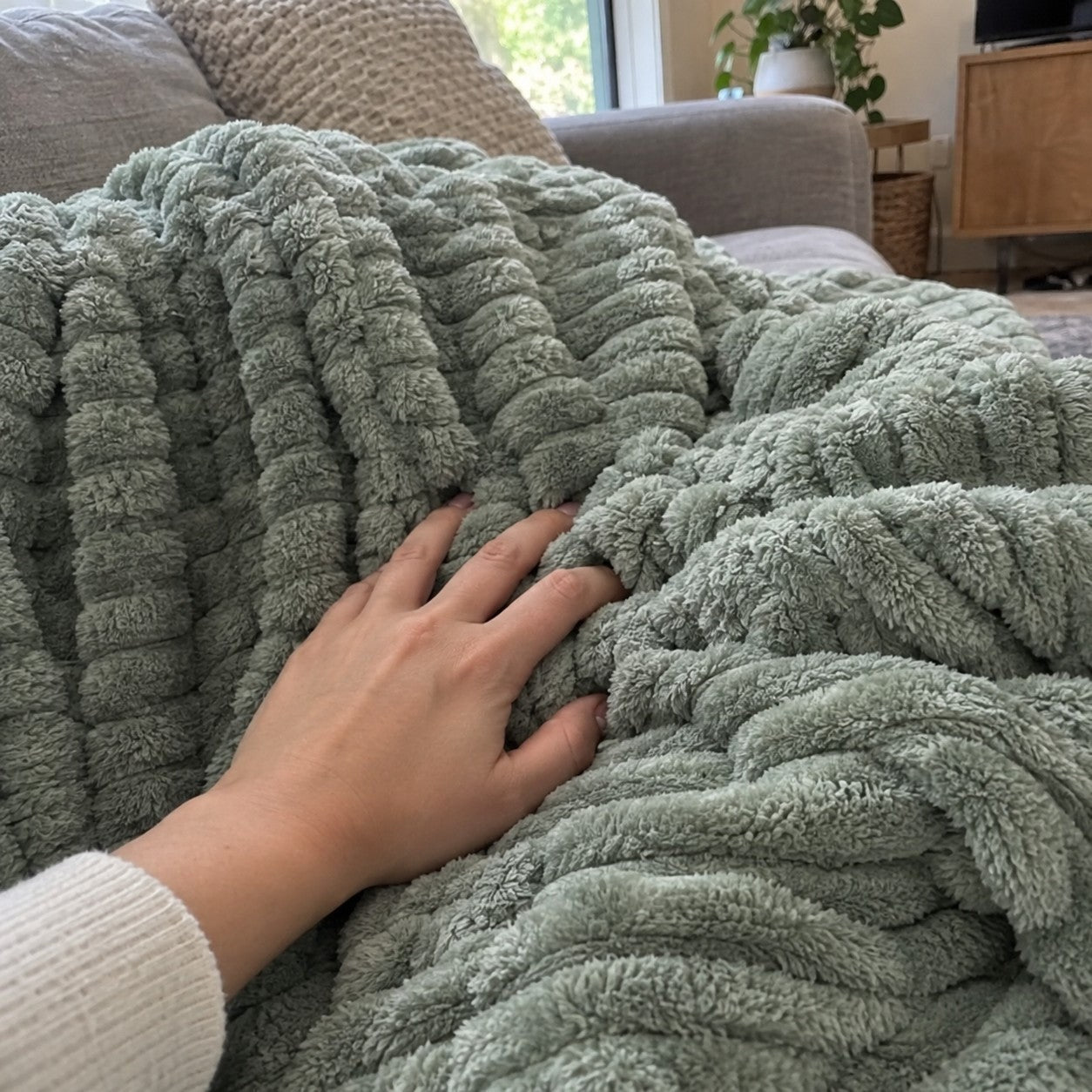 Hand sinking into raised sage green ribs on a sofa