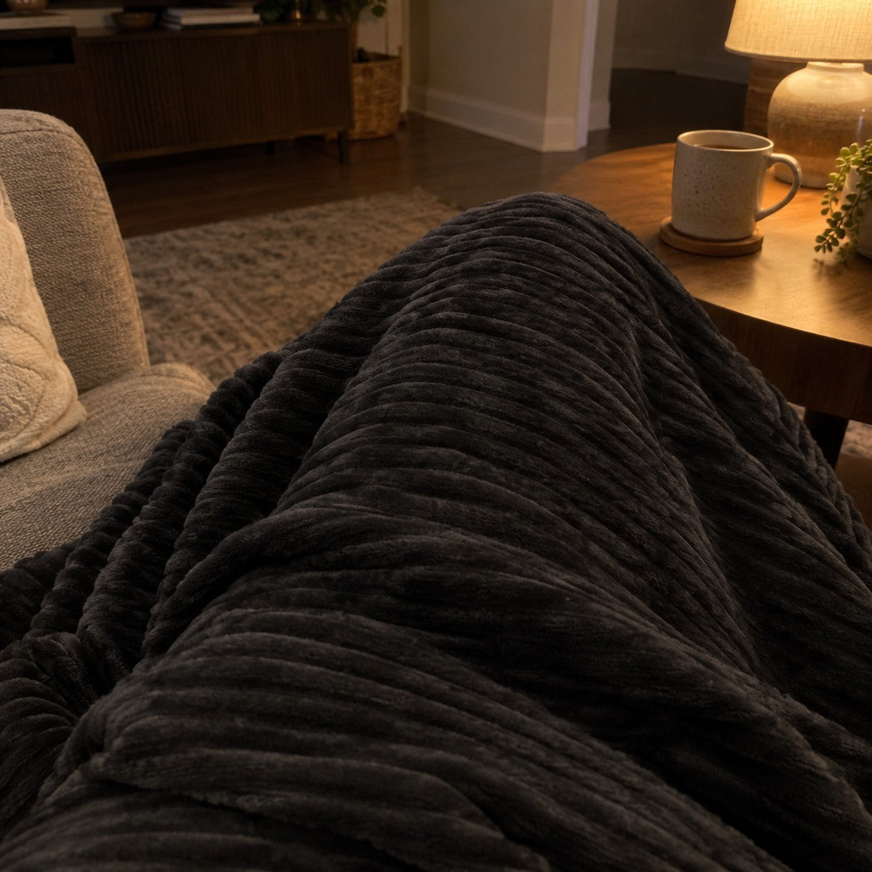Charcoal blanket over a lap beside a mug and lamp