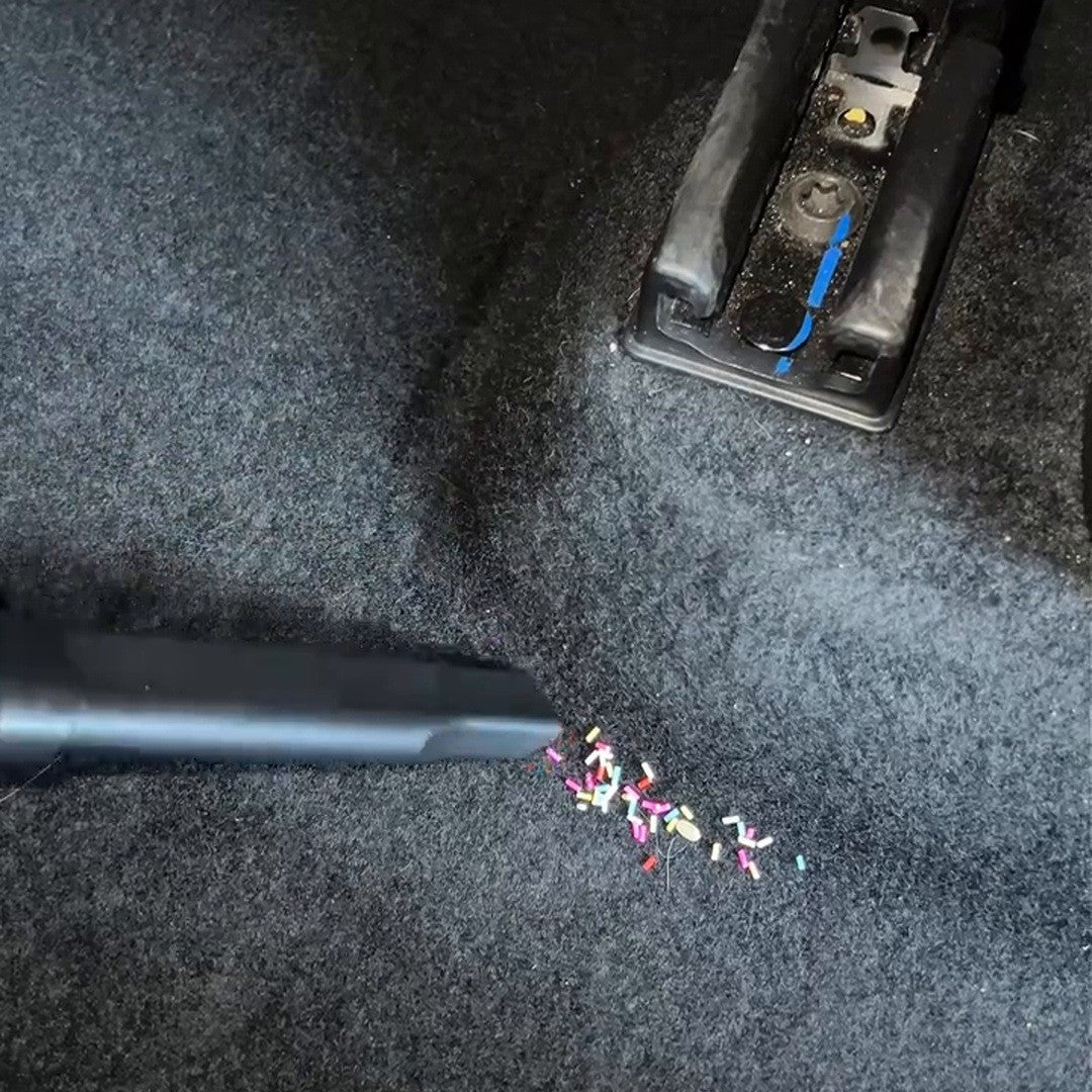 Vacuum nozzle picking up crumbs on dark car carpet