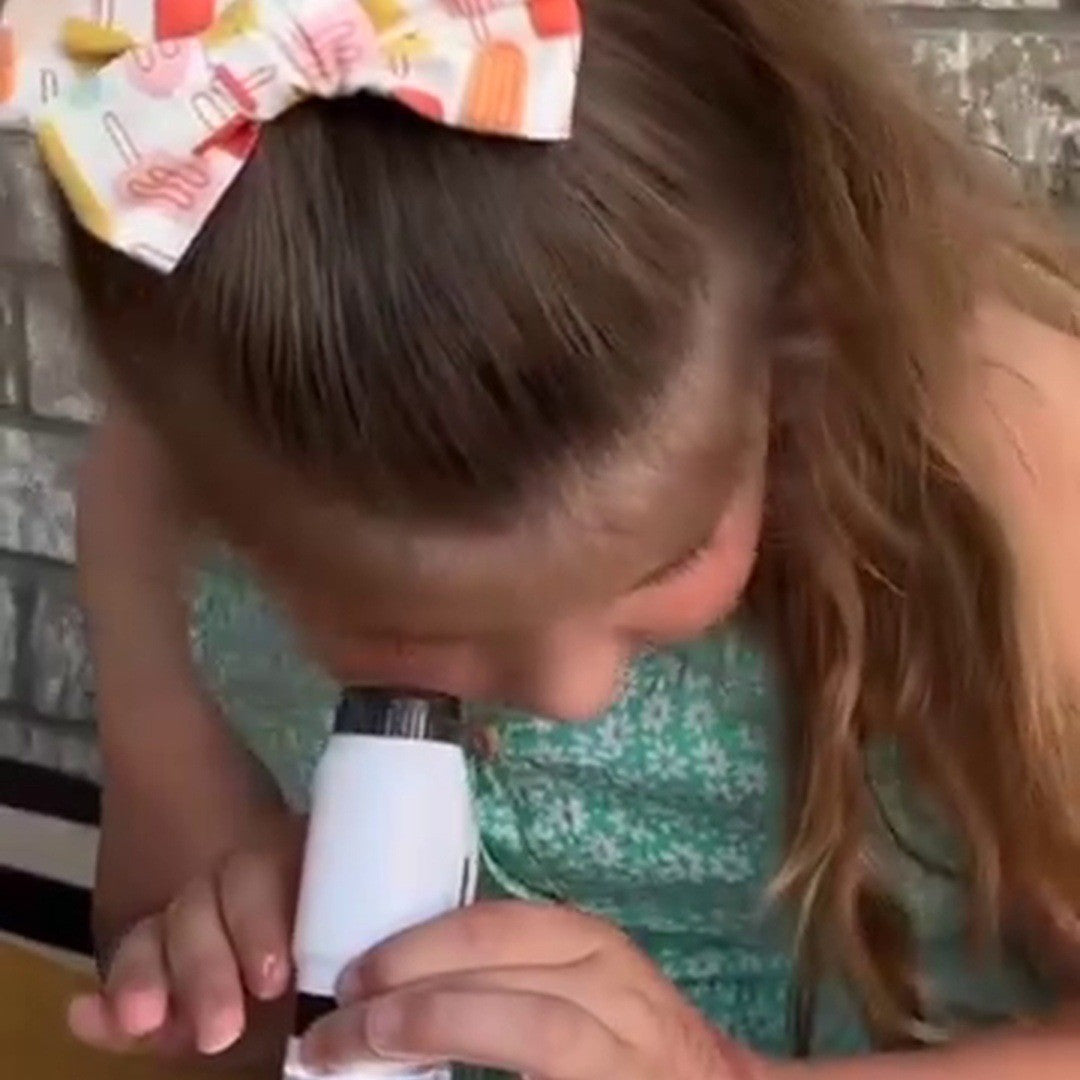 Girl with a hair bow at a microscope on a table