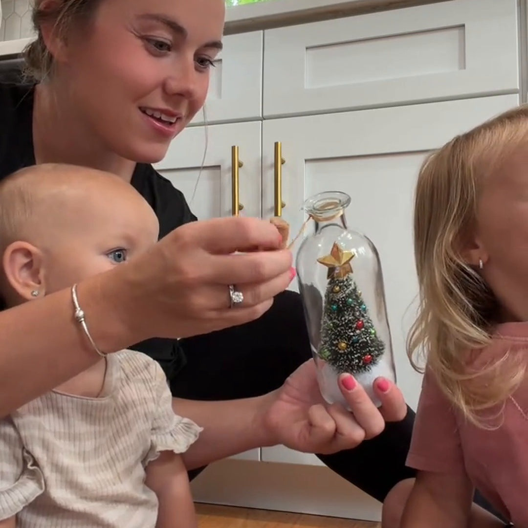 A mother opens the bottle beside her children in a kitchen, showing the tree inside