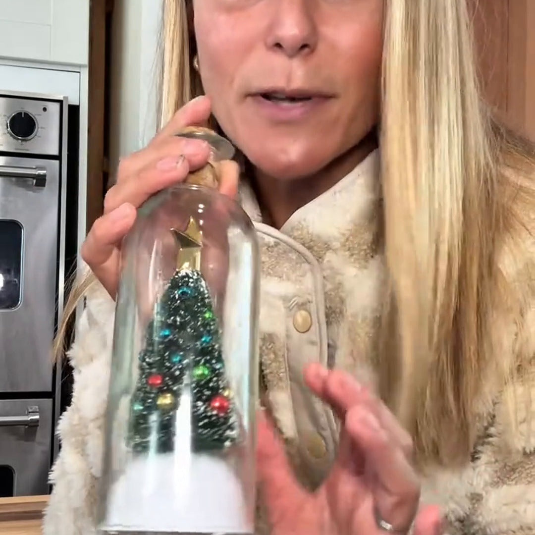 A blonde woman holds the bottle close to her face in her kitchen