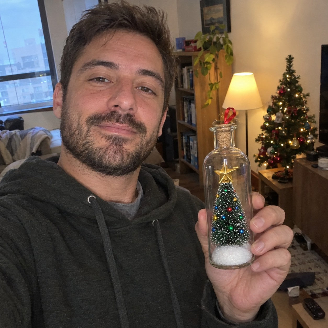 Jake M., a man with short dark hair and beard, holding one matching bottle beside a small Christmas tree