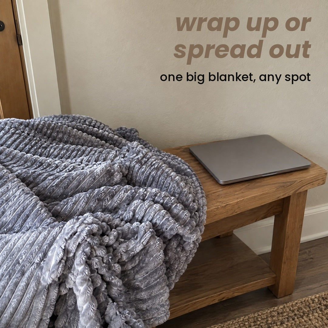 The Grey ribbed blanket in loose folds on a wooden bench beside a closed laptop, headline words at the top right