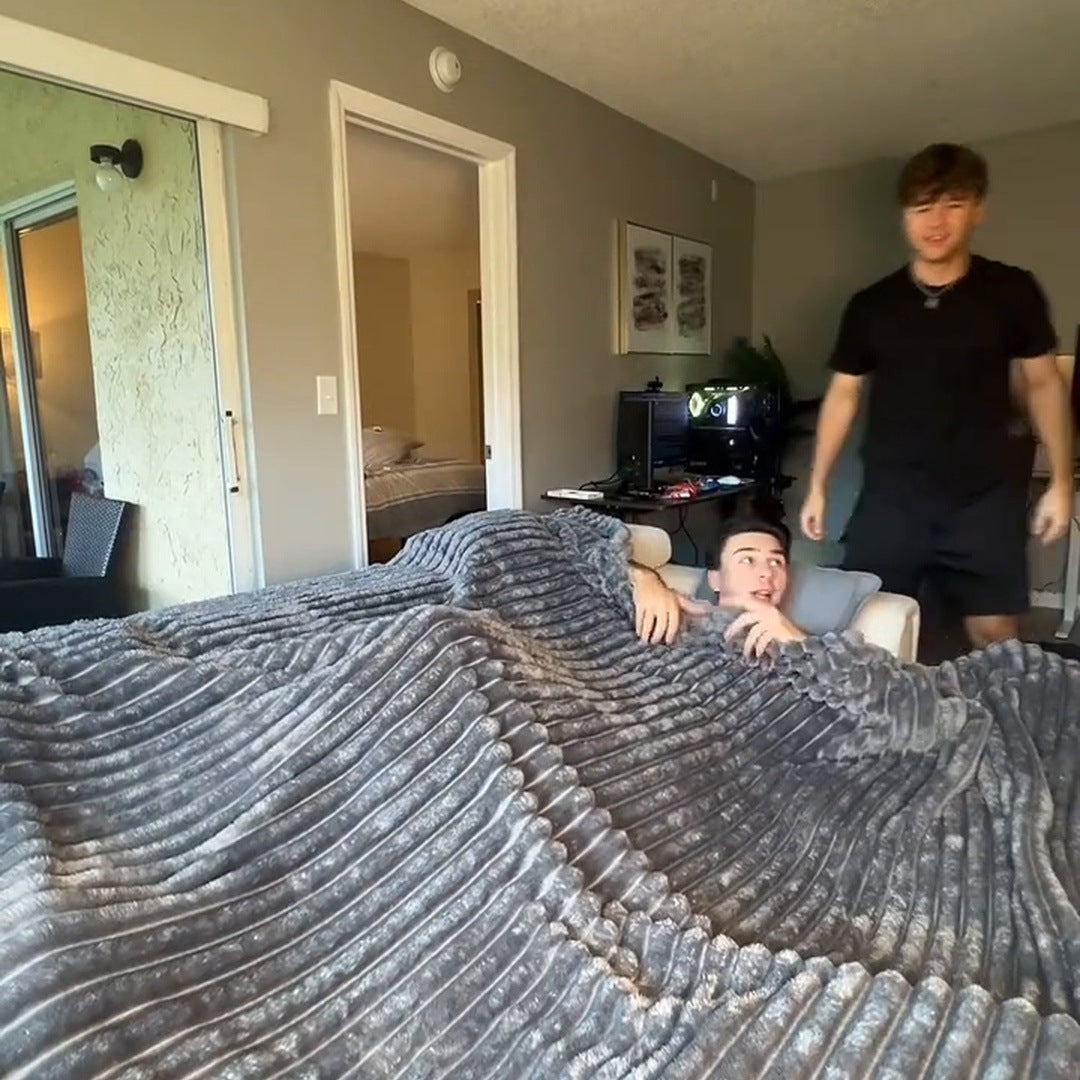 Two young men in an apartment, one resting under the large Grey ribbed blanket spread over a couch