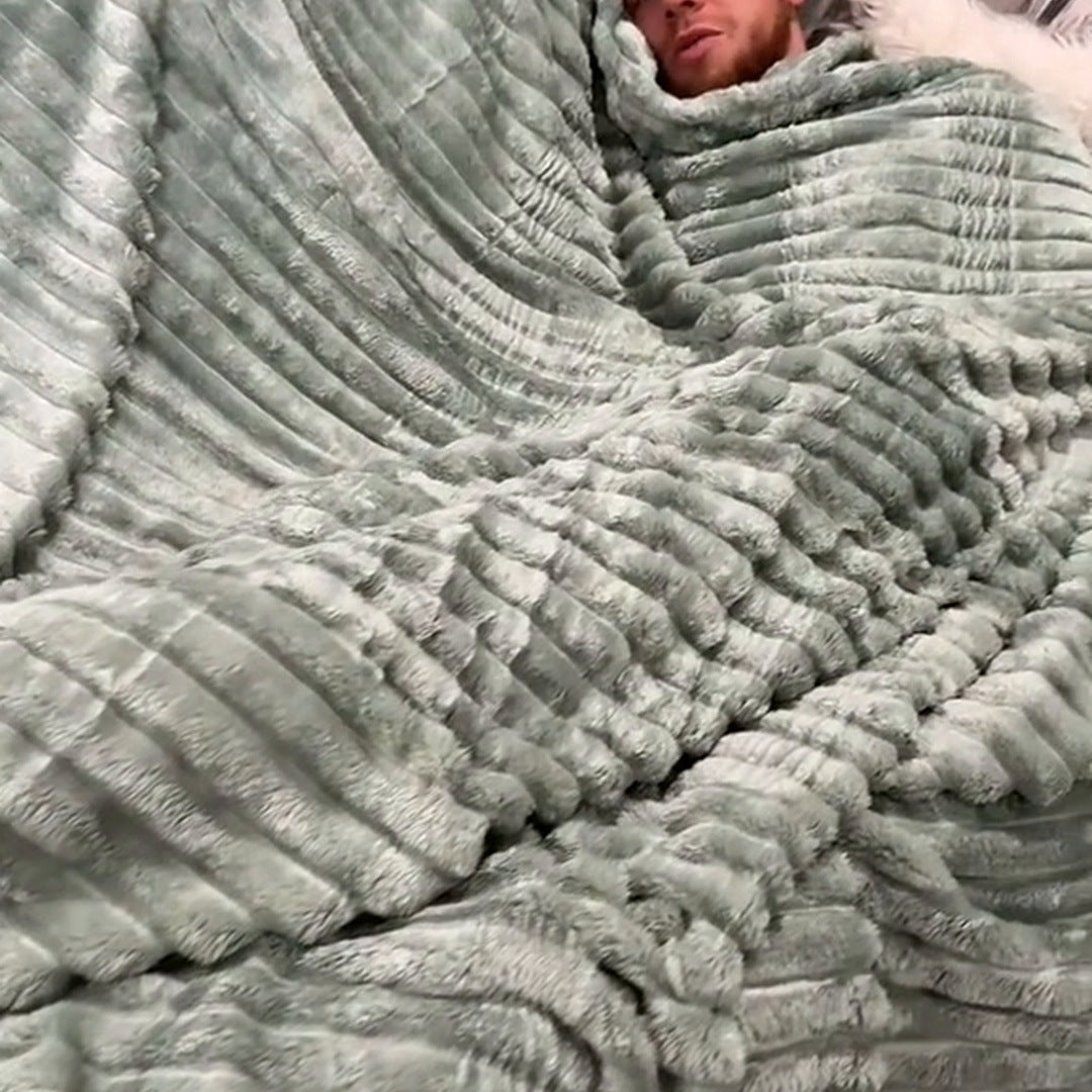The Sage ribbed blanket wrapped around a man resting on a couch, texture in the foreground