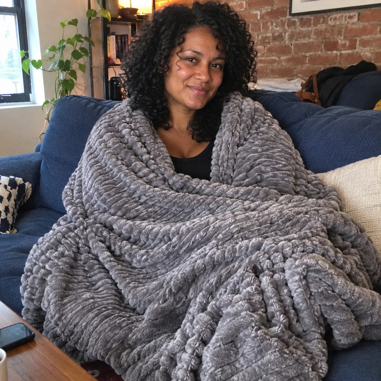 Maya on a blue couch wrapped in the Grey ribbed plush blanket