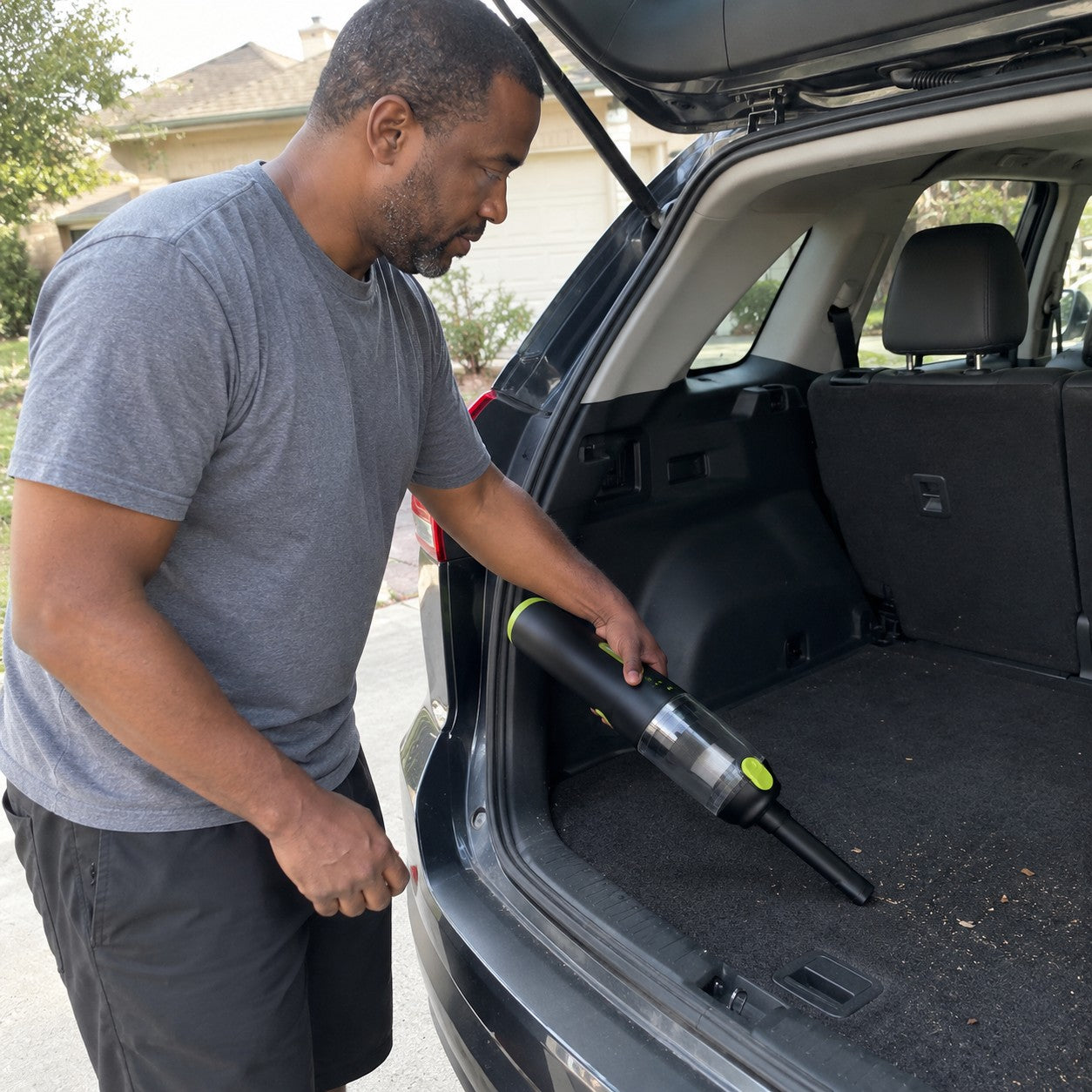 A man uses the cordless black and lime cylindrical vacuum at the open trunk, with the straight nozzle at its clear-cup front