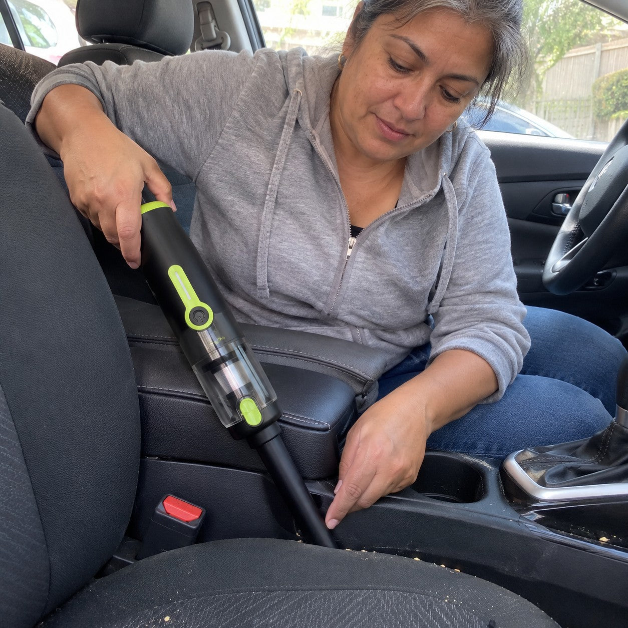 Adult woman cleans a car-seat seam with the straight nozzle attached to the clear dust-cup front