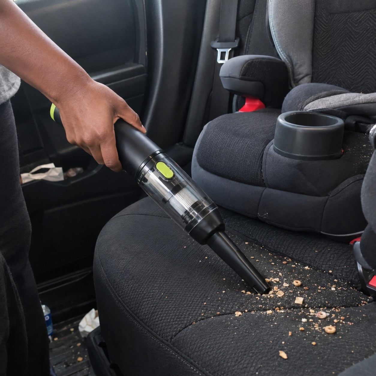 A dark-skinned hand uses the front nozzle to pick up loose crumbs on a child car seat