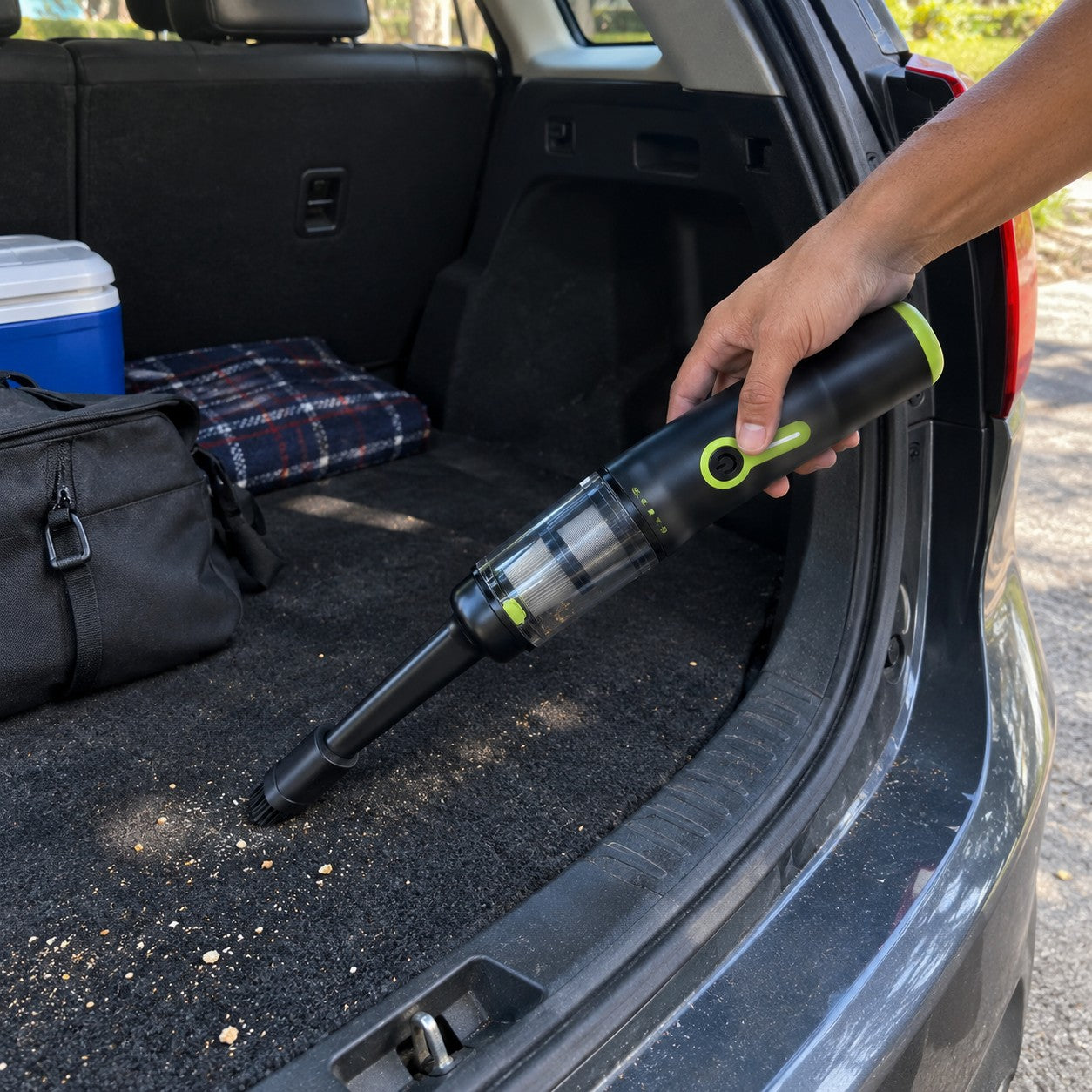 Hands clean trunk debris with the vacuum nozzle attached to the clear-cup front