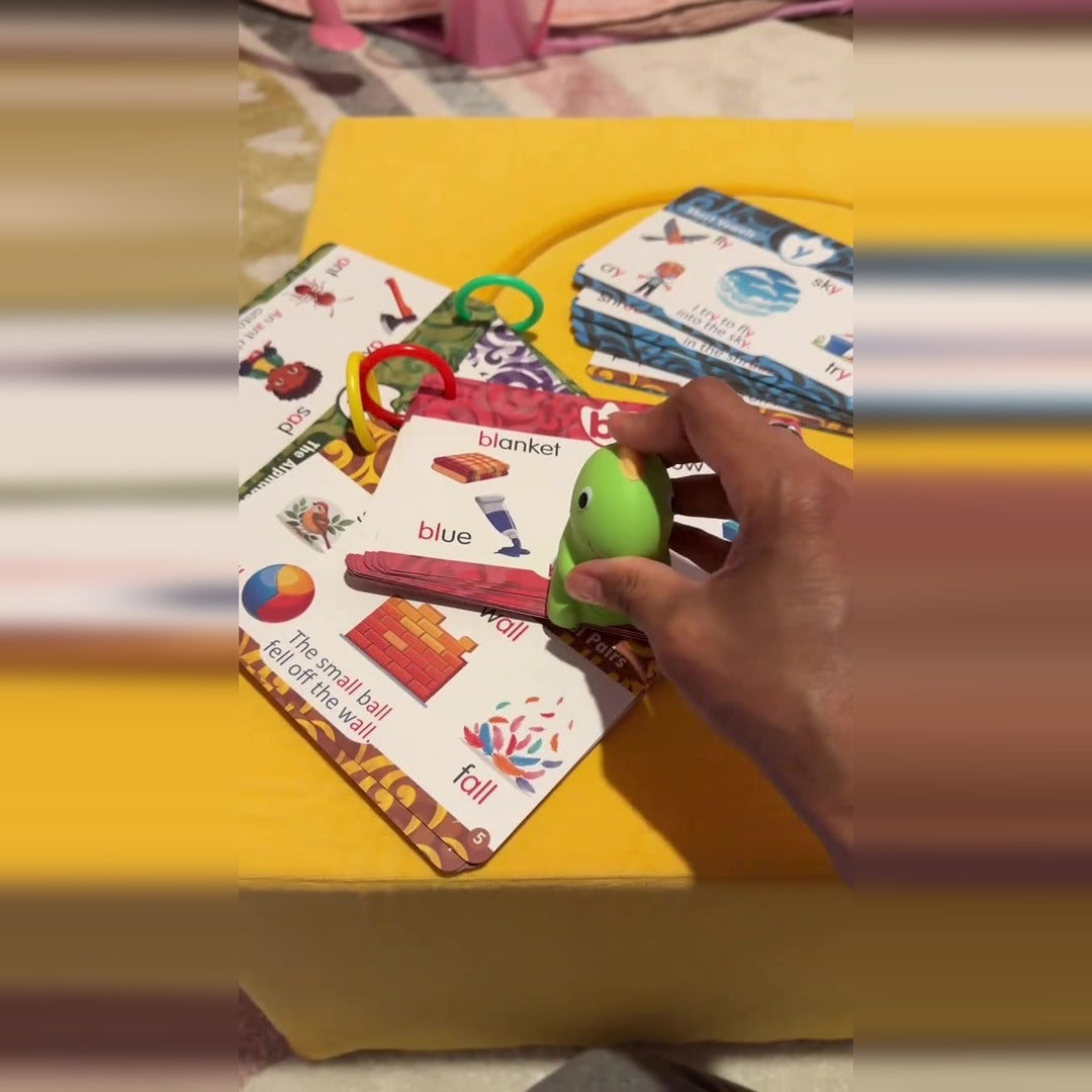 A hand holds the green dinosaur reader above the printed learning cards on a yellow cushion