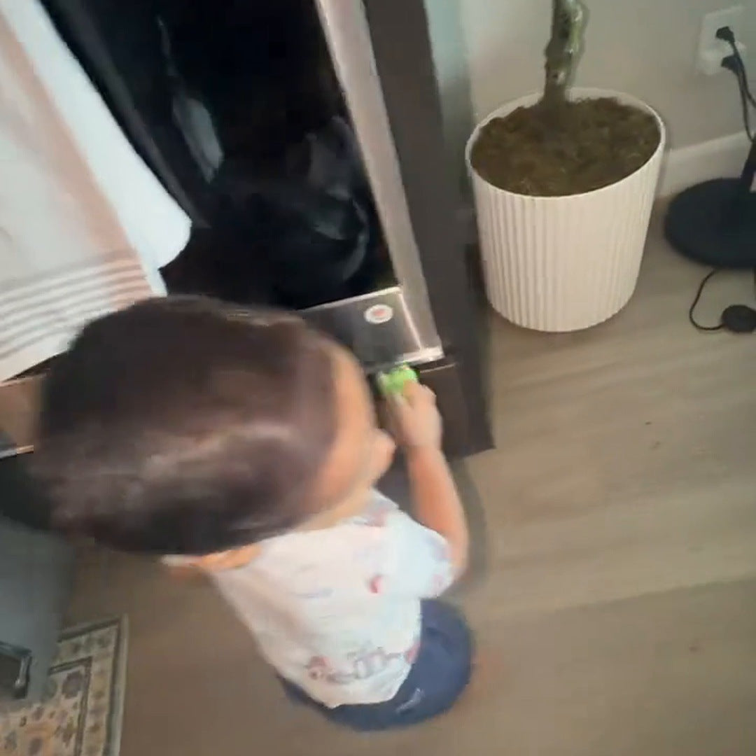 A young boy holds the green dinosaur reader to a sticker on the water dispenser at home