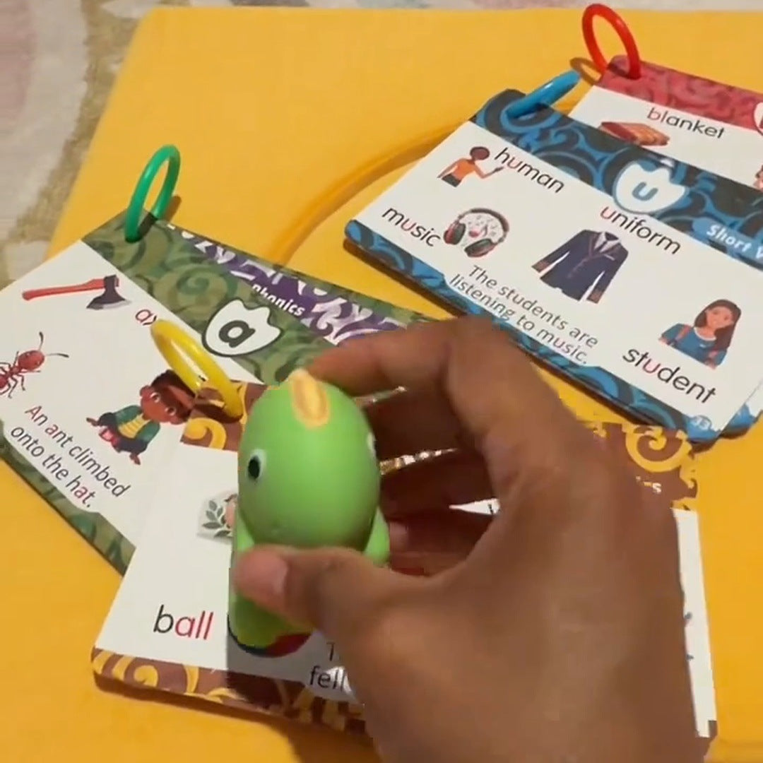 A hand taps the green dinosaur on a picture card on a yellow cushion