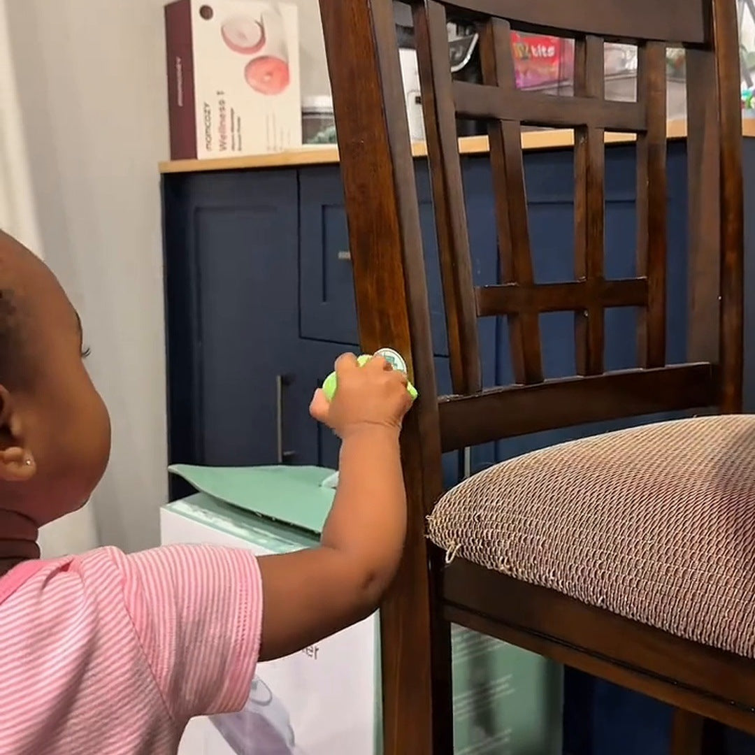 A little girl in a pink top holds the green reader against a chair sticker at home