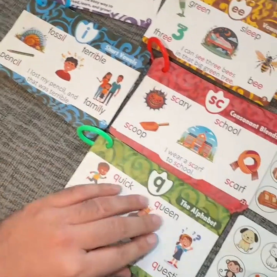 Printed phonics and alphabet cards with colored borders and organizing rings spread across a sofa