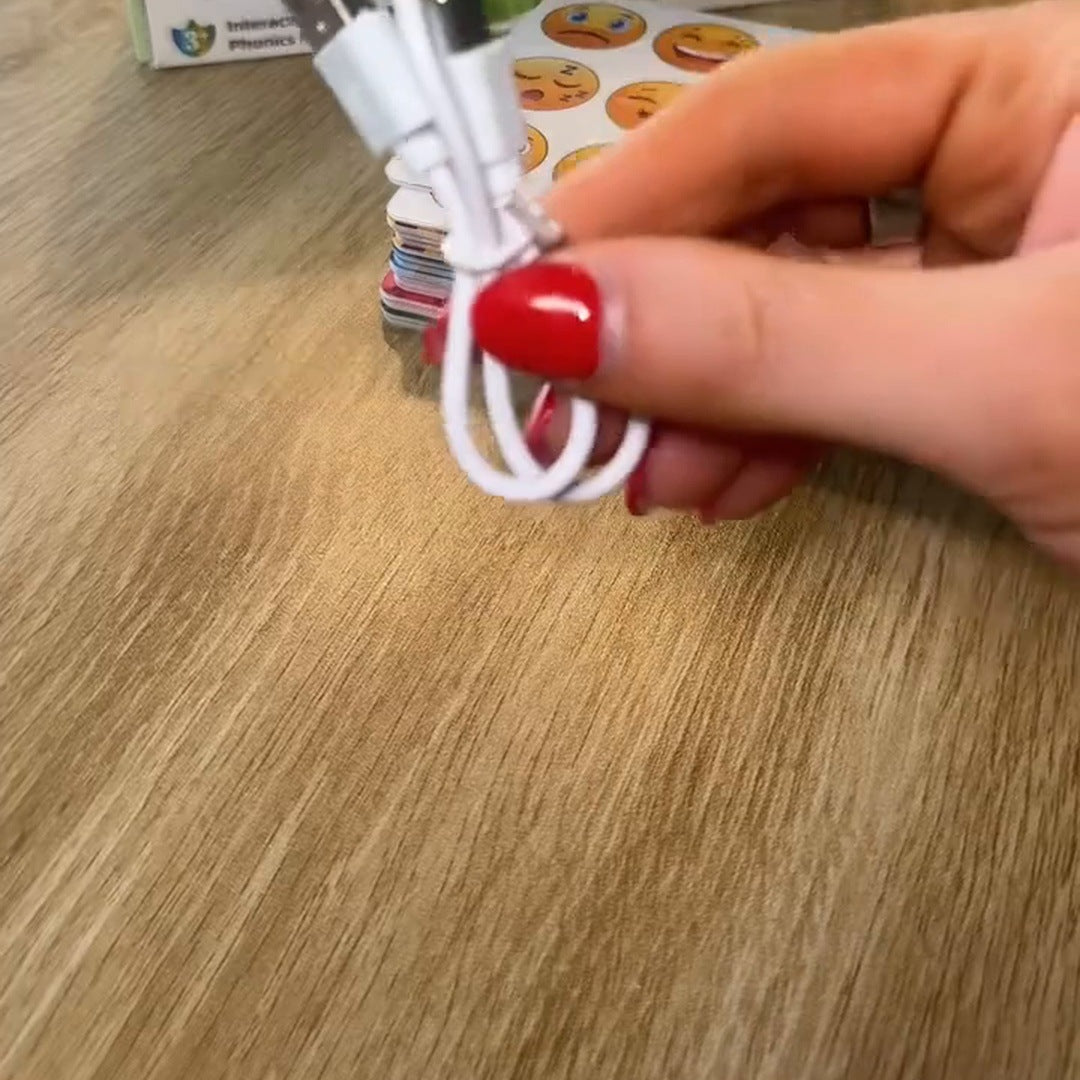 A hand shows the included white charging cable over the wooden table