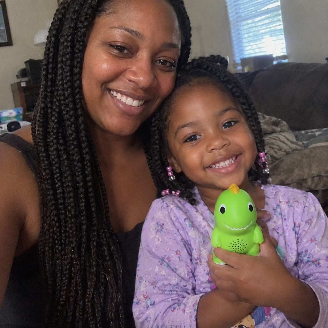 Monique with box braids smiles beside her daughter, who holds the green dinosaur at her chest