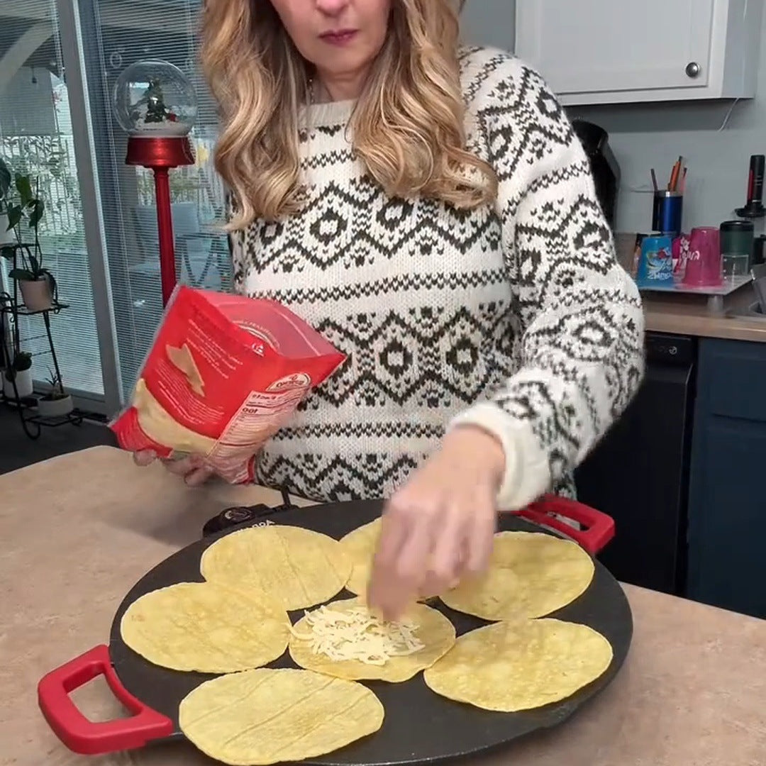 Real blonde creator in a patterned sweater placing cheese on tortillas on the red-handled round grill