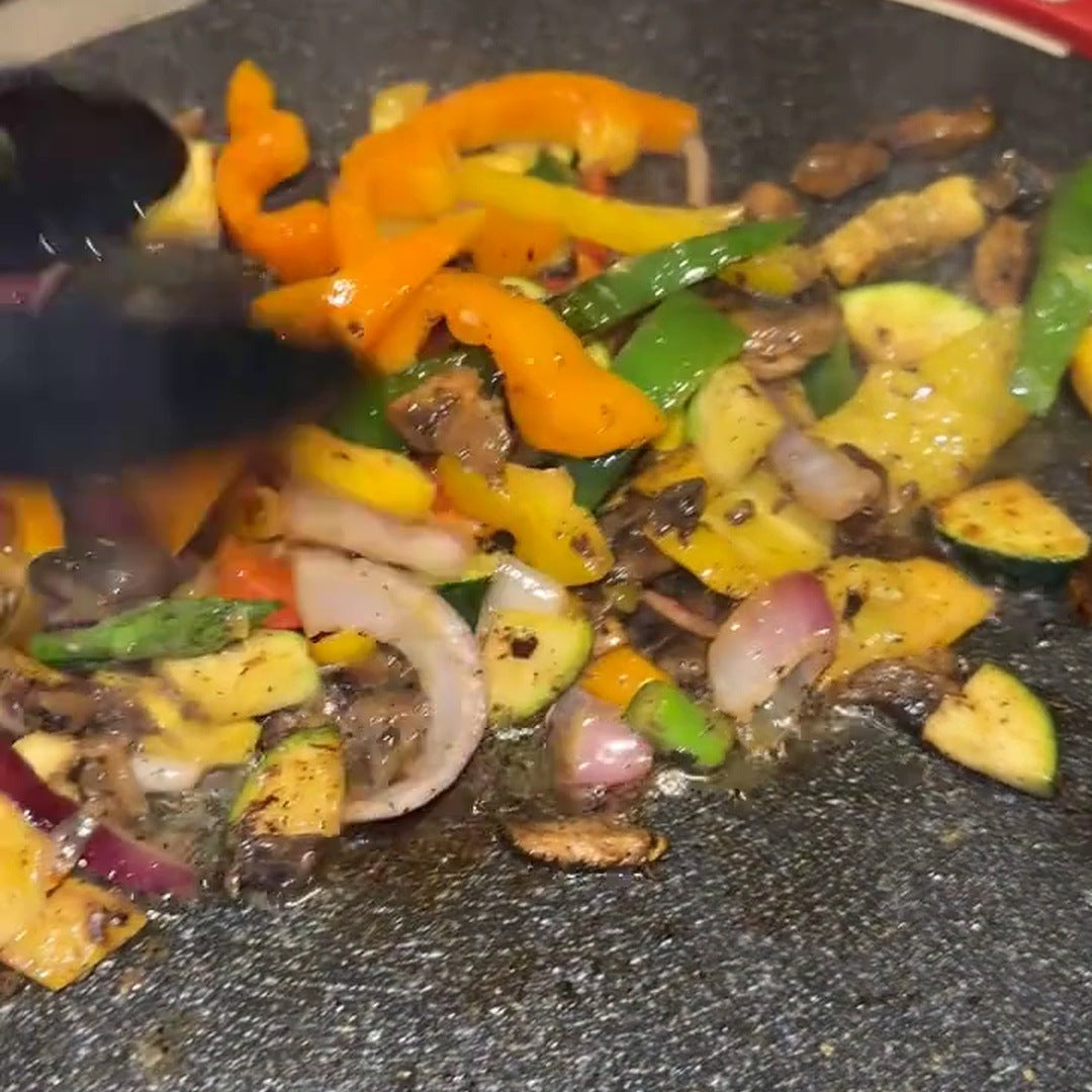 Real chopped peppers, zucchini, onion and mushrooms being stirred on the flat speckled cooking surface
