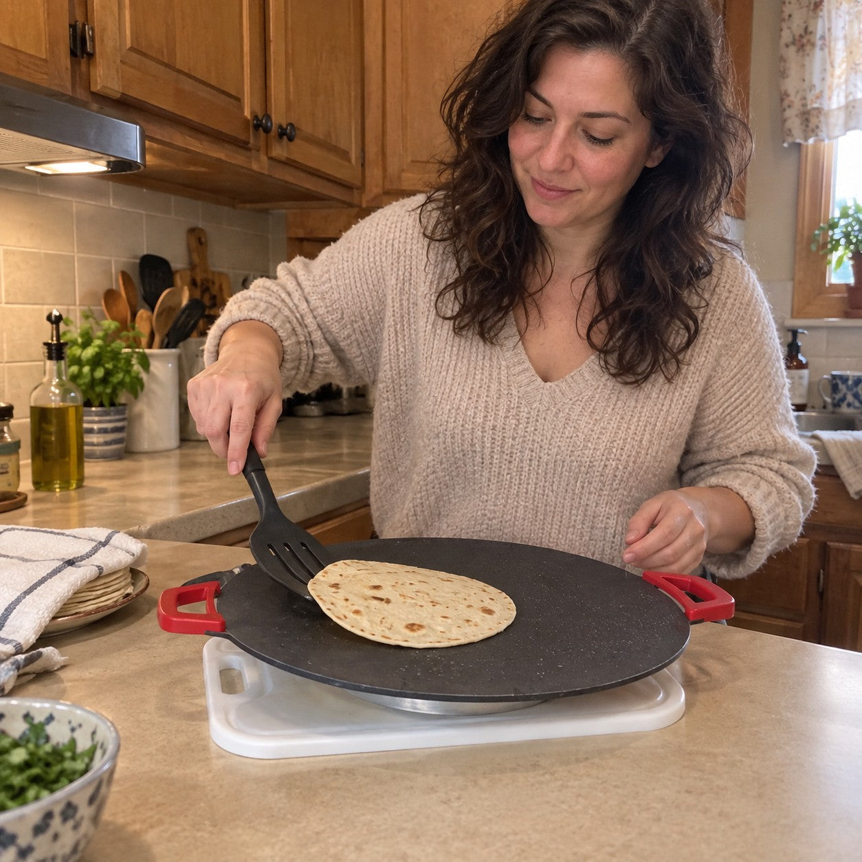 Elena M.: light skin, wavy dark brown hair and cream sweater, using a spatula on a tortilla on the red-handled grill