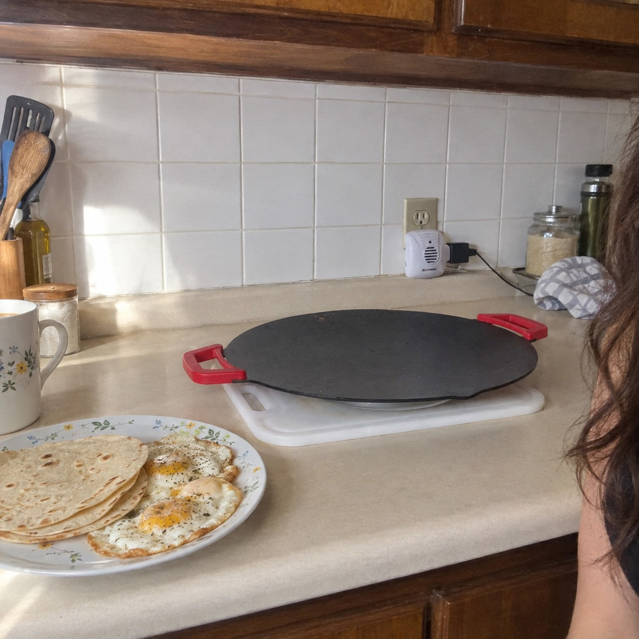 A plate of eggs and tortillas beside the same red-handled round grill in Elena M. kitchen