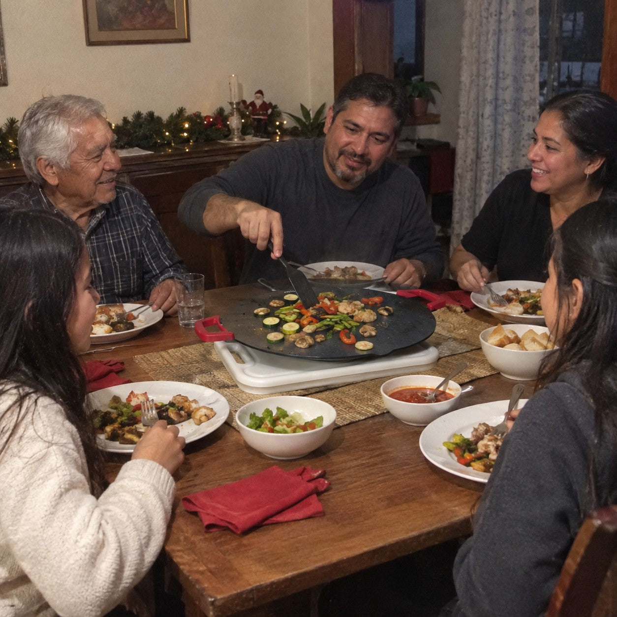 A father cooks at the family table with older relatives and children seated around him, holiday greenery in the room
