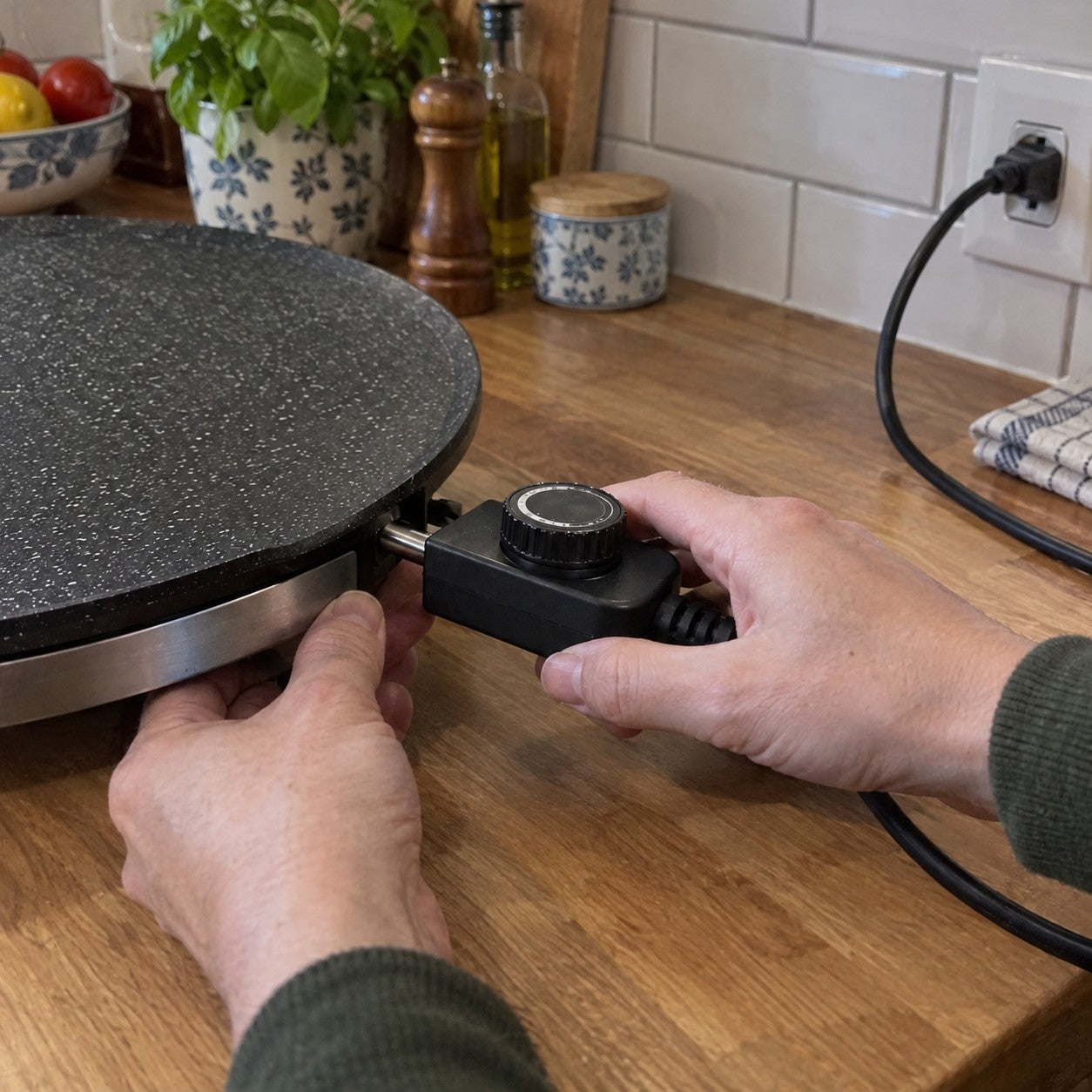 Two adult hands attach the black rectangular controller with its round ridged black dial to the empty grill