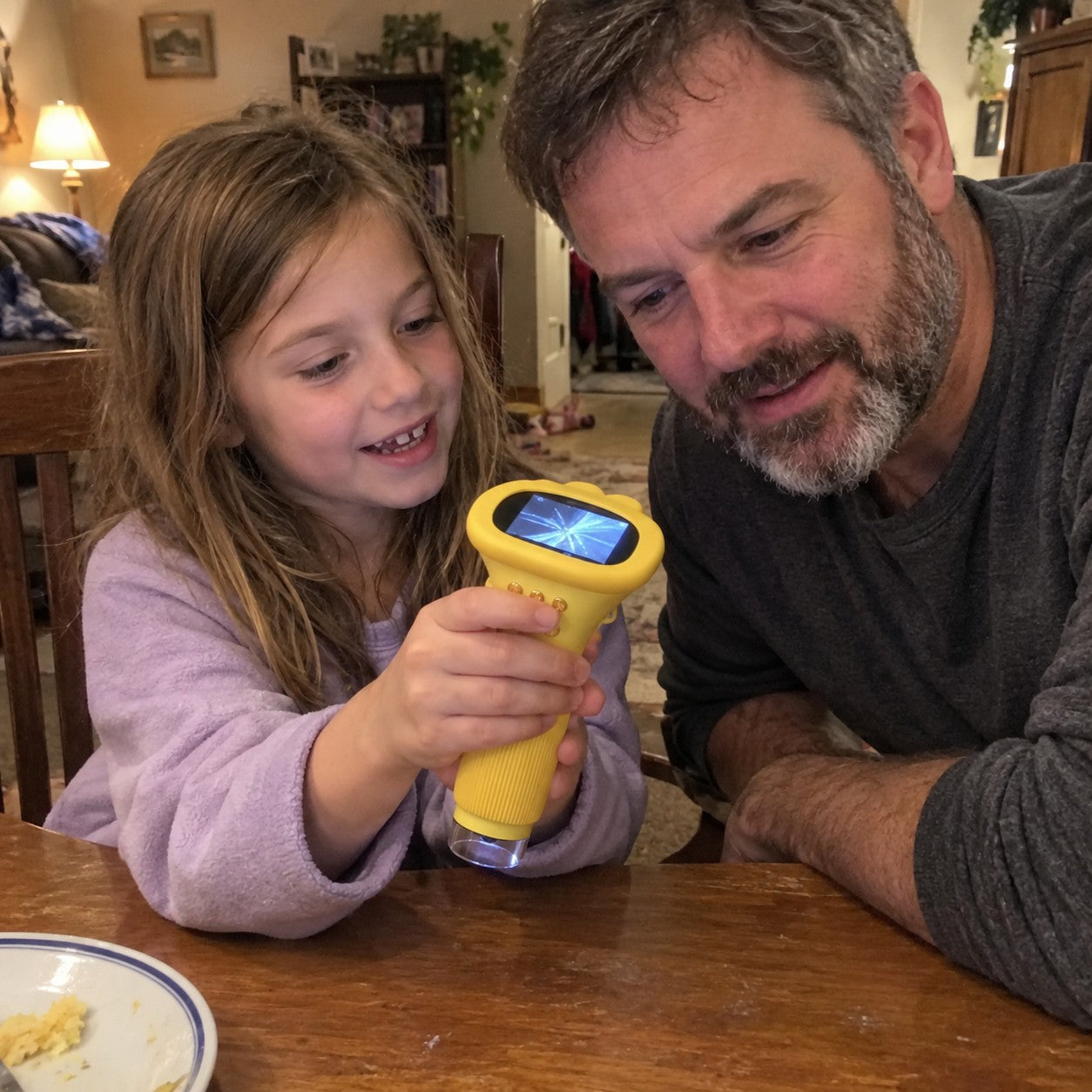 Father and daughter examine the yellow scope together at a dining table, screen shows a blue fiber texture