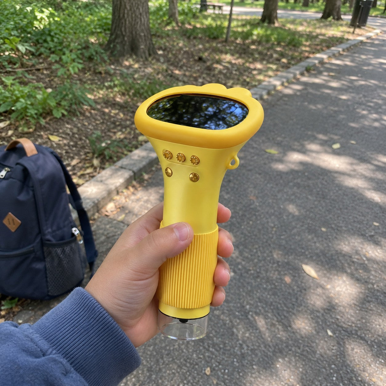Child's hand holding yellow scope on a park path